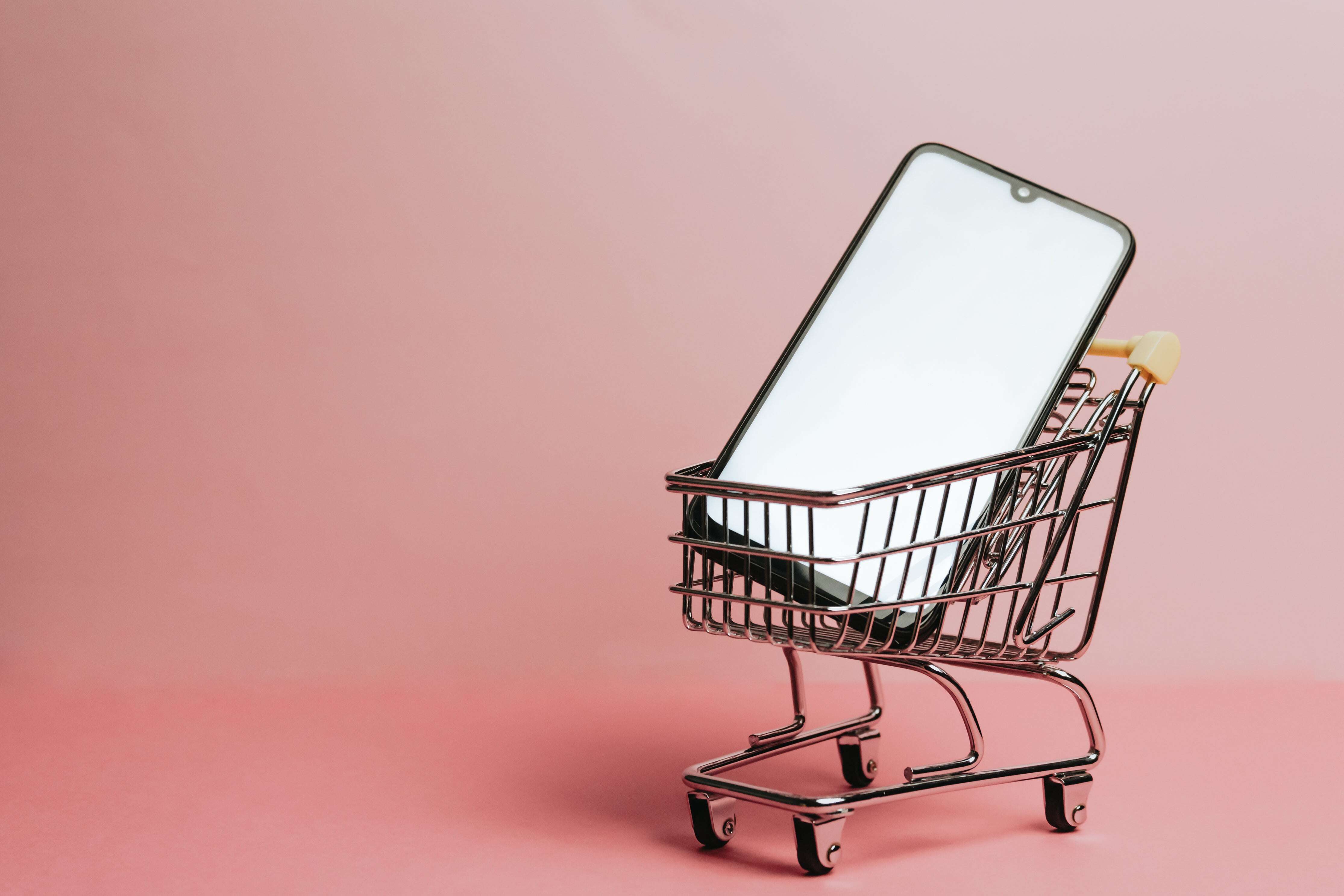 cell-phone-sits-in-a-small-shopping-cart-against-pink